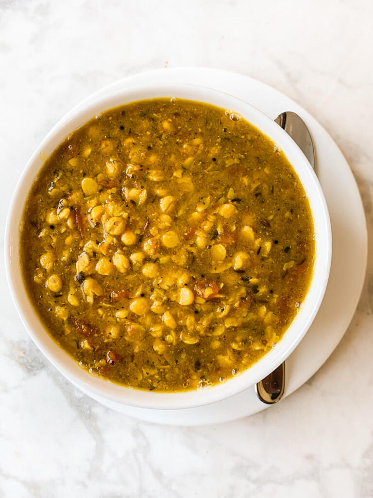 Bowl of dal on a plate with a spoon.