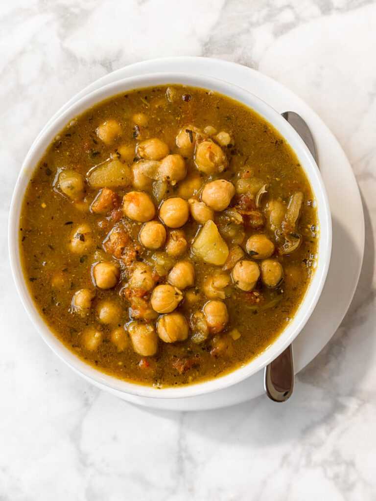 Bowl of chana masala on plate with spoon.